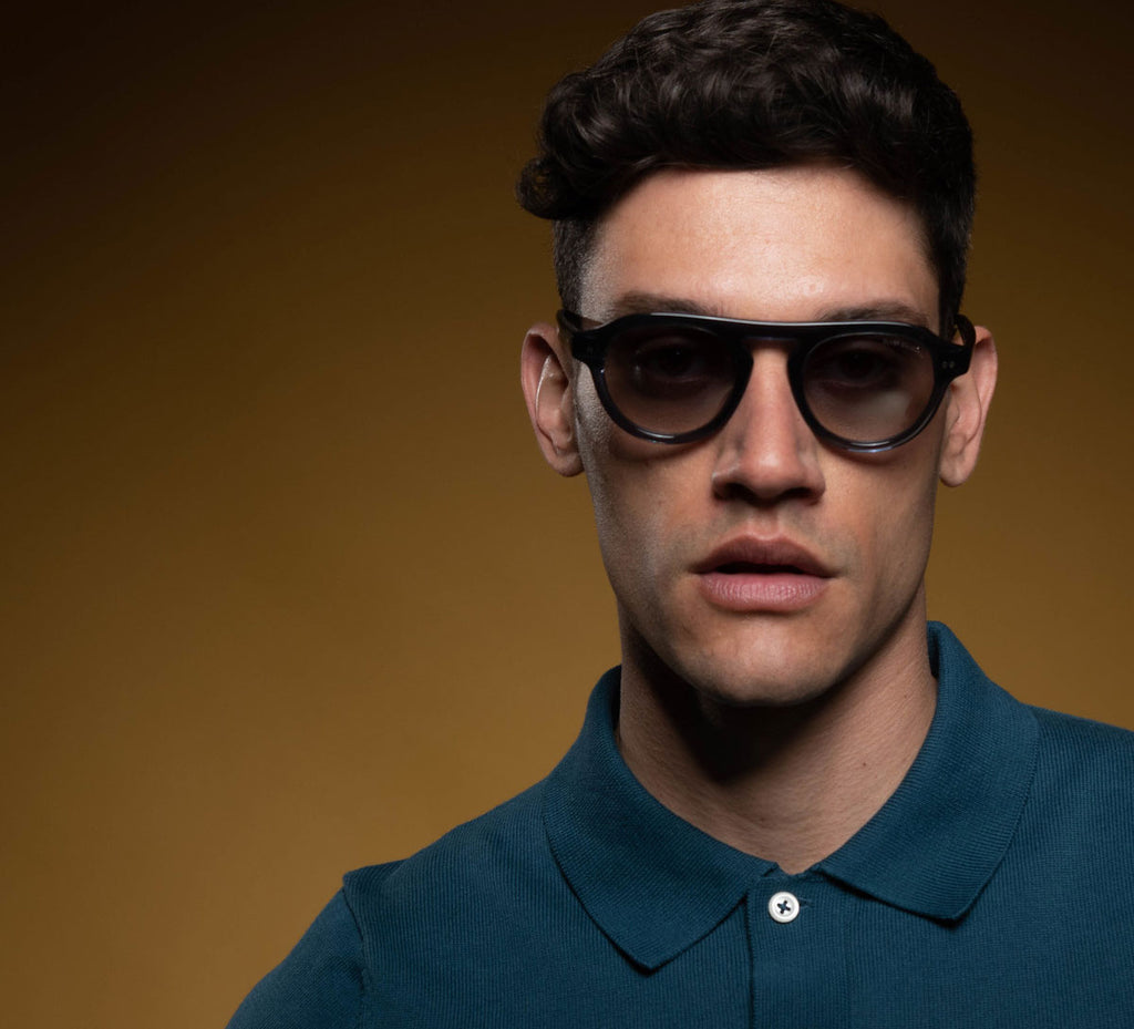 A Male Model looking directly at the camera wearing oliver goldsmith sunglasses with semi tinted lenses